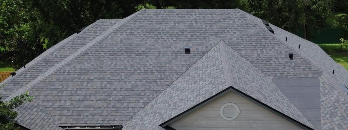 Front gable with a round louvered vent below long hipped planes of new shingles in Alachua