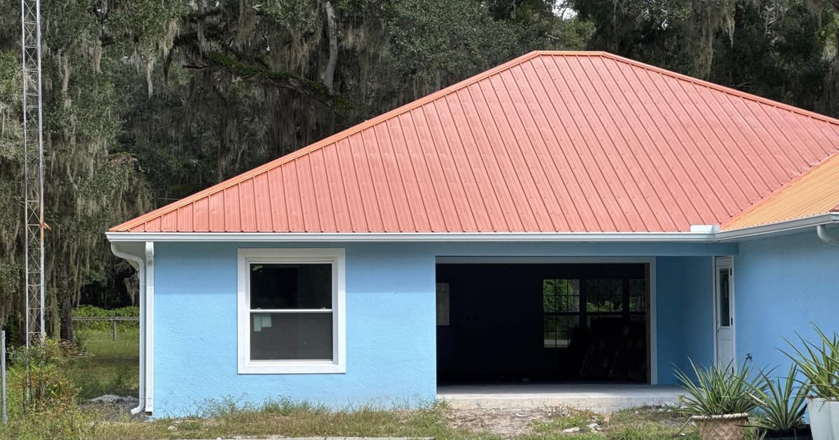 Terracotta orange metal hip roof over a sky blue home in Anthony, framed by mossy oaks