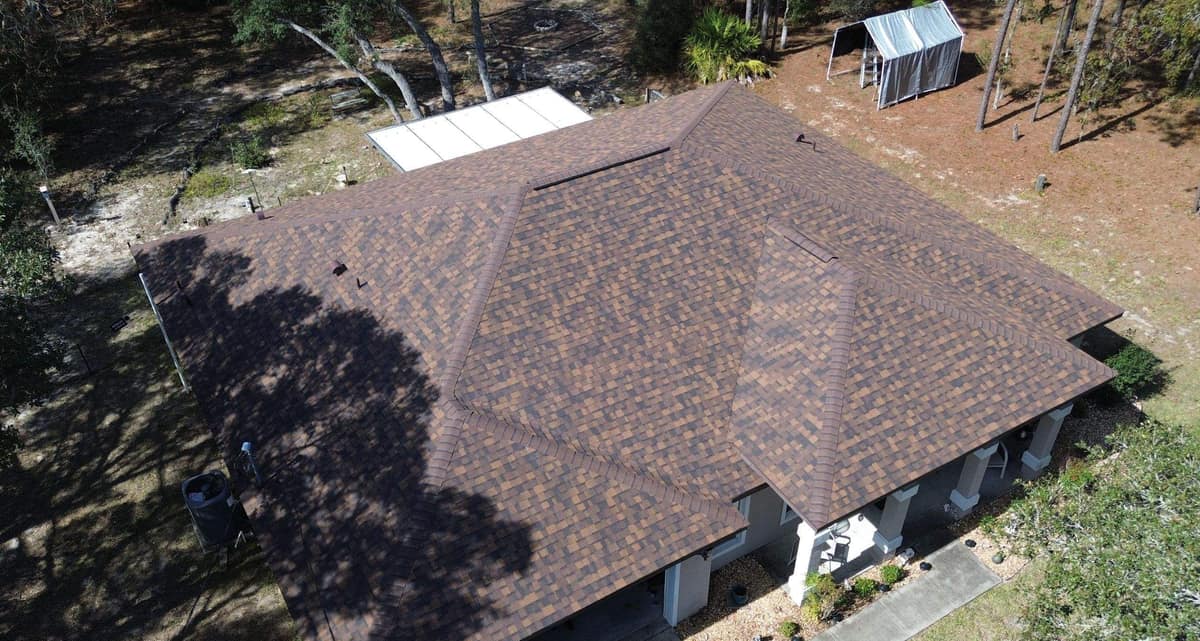 Drone view over a Dunnellon stucco home with a new brown and tan shingle hip roof