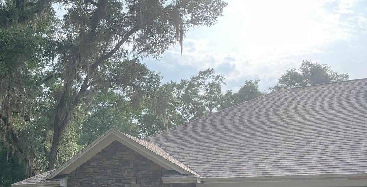 Stacked stone front gable under the new shingle roof in Gainesville, beside a moss-draped oak