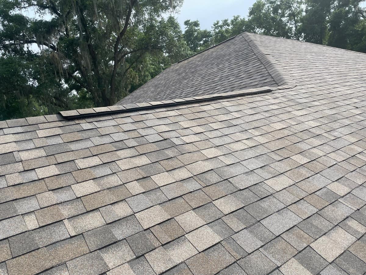 Ridge vent under ridge cap shingles in front of a taller hip section of the Gainesville roof