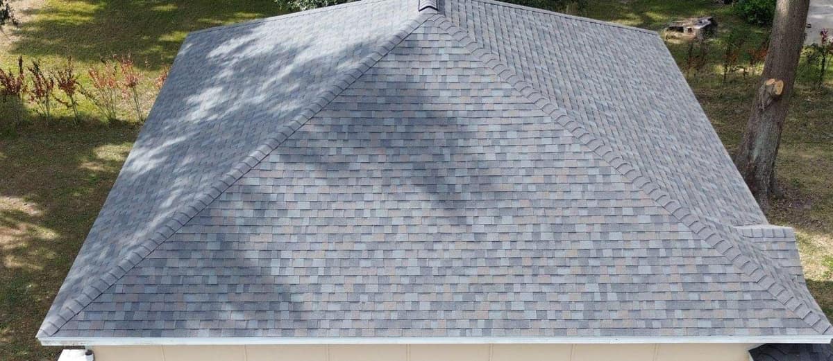 Drone view of the two-story hip roof in Lake City with new gray blend shingles under oak shade