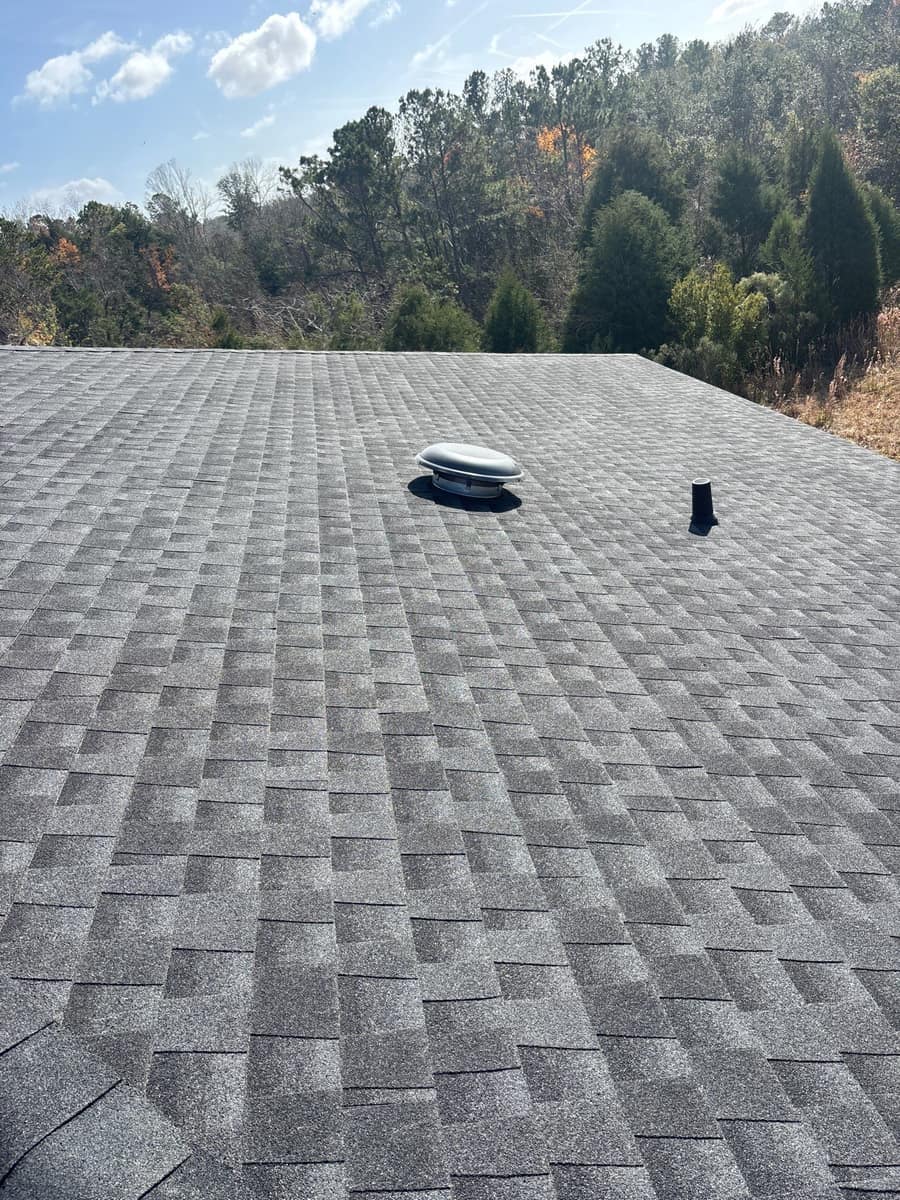 Round metal roof vent and a plumbing pipe on a slope facing woods in Live Oak