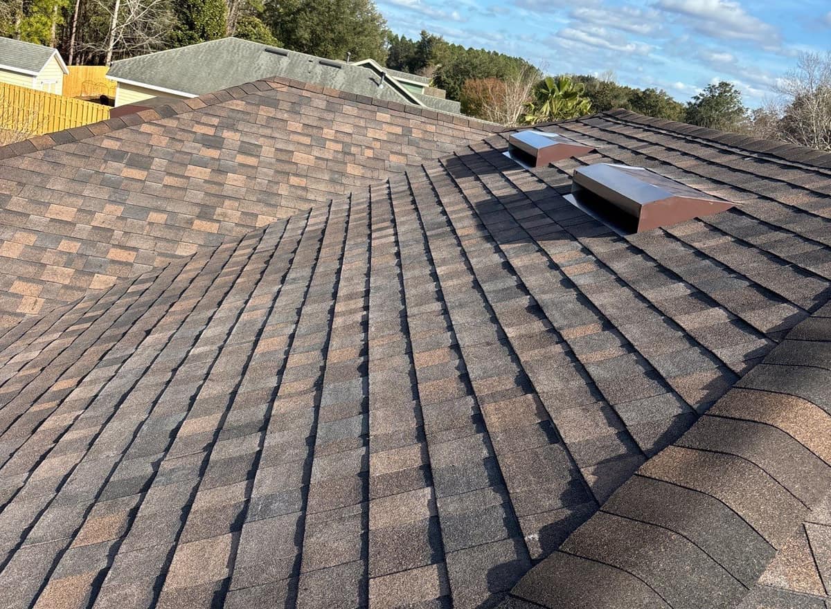 Rooftop view of new brown blend architectural shingles, hip caps and two box vents in Newberry