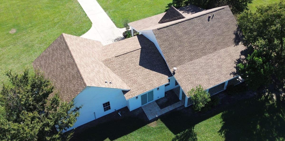 Drone view of the back of an Ocala farmhouse and its garage wing under new light brown shingles