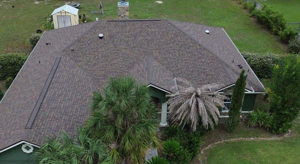 Drone view of a new brown shingle hip roof on a green stucco home in Ocala