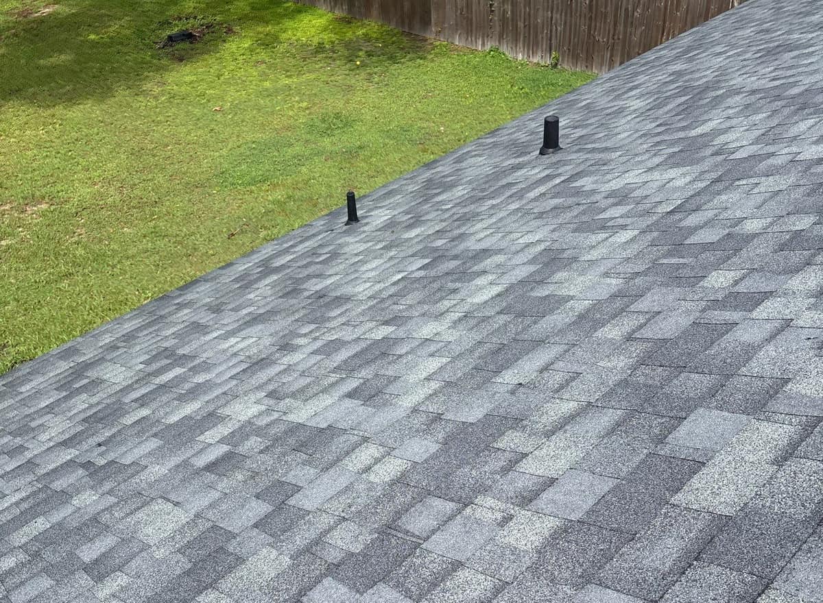 New gray architectural shingles and two black vent pipes on the slope above a fenced lawn in Ocala